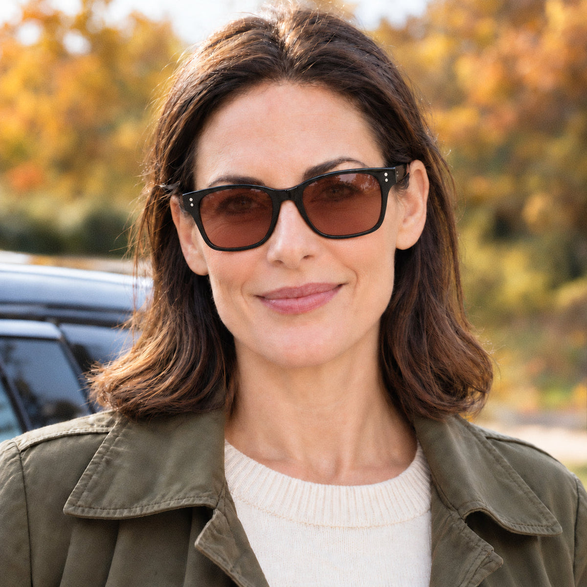 A woman wearing Eyelevel-UK Cruiser driving sunglasses with black frames and warm-tinted lenses outdoors.