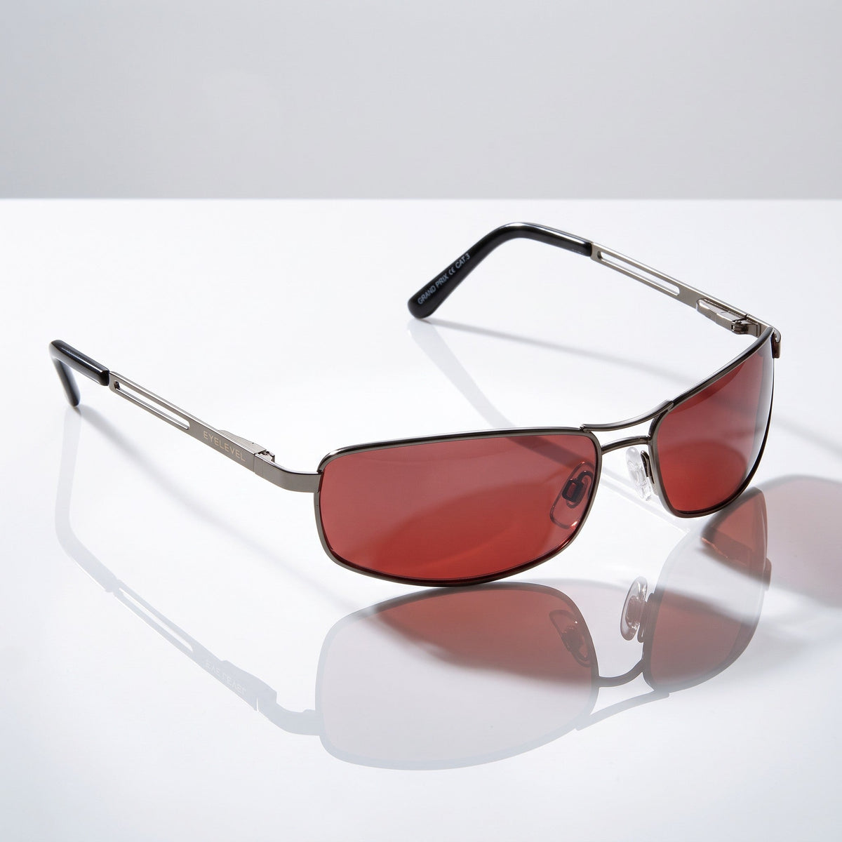 Eyelevel-UK Grand Prix driving sunglasses with gunmetal frames and high density red-tinted lenses on a white surface.
