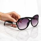 Eyelevel-UK Hayley oversized black sunglasses with silver stone detail and grey gradient lenses held by a hand.