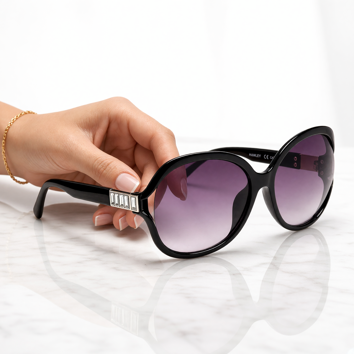 Eyelevel-UK Hayley oversized black sunglasses with silver stone detail and grey gradient lenses held by a hand.