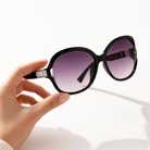 Eyelevel-UK Hayley oversized black sunglasses with silver stone detail and grey gradient lenses held in a hand