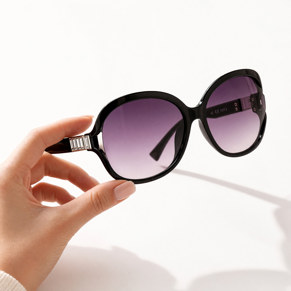Eyelevel-UK Hayley oversized black sunglasses with silver stone detail and grey gradient lenses held in a hand