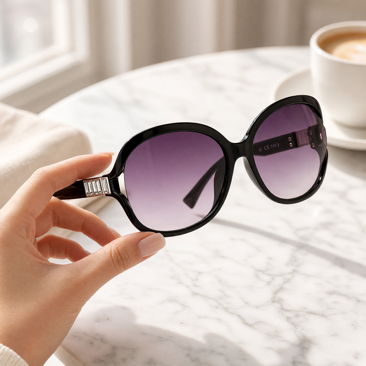 Eyelevel-UK Hayley oversized black sunglasses with silver stone detail and grey gradient lenses held by a hand.
