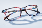 Eyelevel-UK Martinique reading glasses with a multicolour floral square plastic frame on a reflective surface.